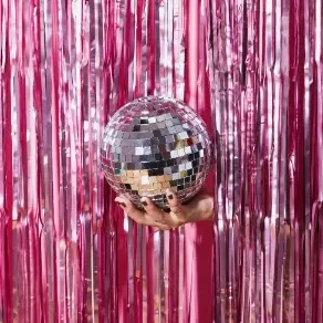 Hand holding a disco ball with a shiny pink tinsel background.